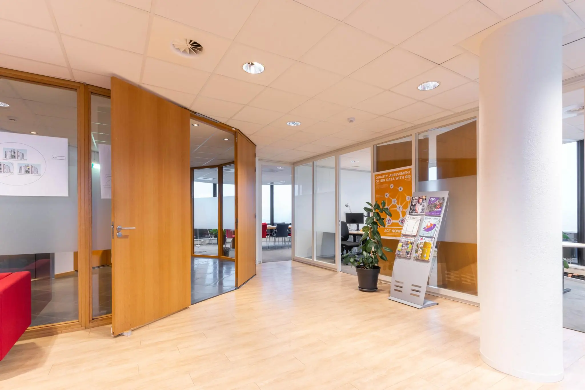 Moderne kantoorruimte aan de 1e Hogeweg met glazen wanden, houten deuren, een tijdschriftenrek en een kamerplant.